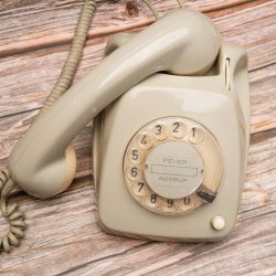 Retro rotary phone with dial on rustic wooden surface, nostalgic feel.